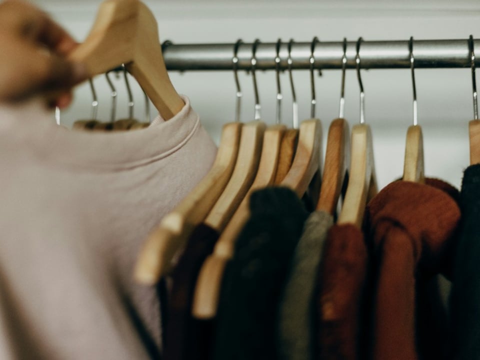 Mano eligiendo una prenda en un perchero con ropa organizada en percheros de madera