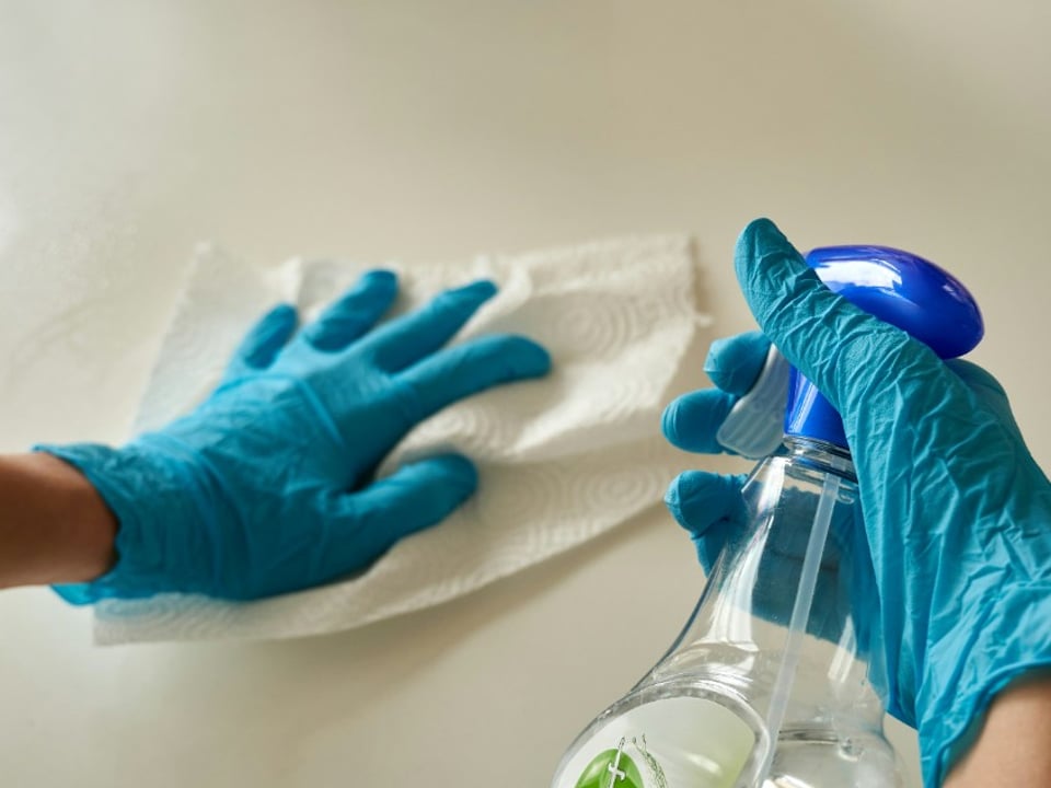Manos con guantes limpiando una superficie con paño y spray desinfectante